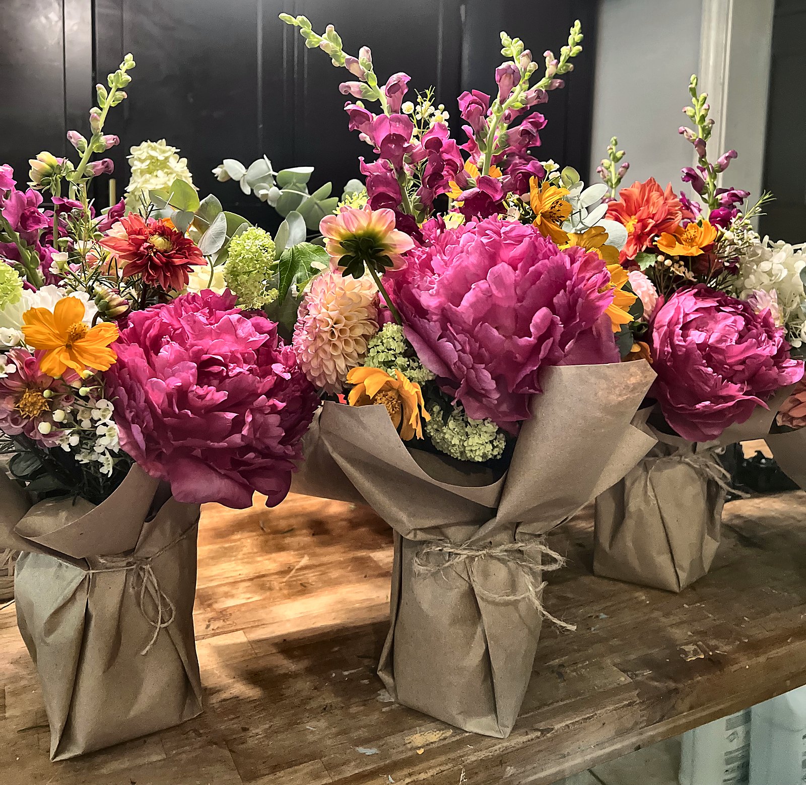 Wrapped bouquets of pink peonies, snapdragons, dahlias and orange cosmos tied with twine