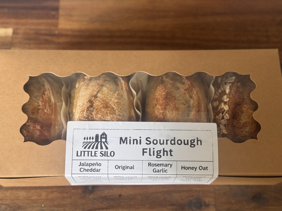 A kraft box of four mini sourdough loaves with a Little Silo label reading Mini-Sourdough Flight: jalapeño cheddar, original, rosemary garlic, and honey oat
