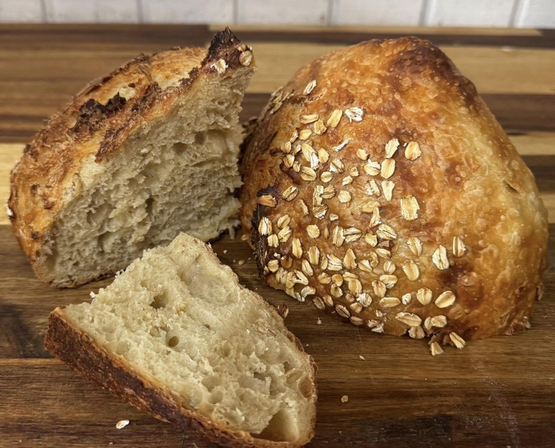 Honey oat sourdough loaf topped with rolled oats, cut open to show the crumb