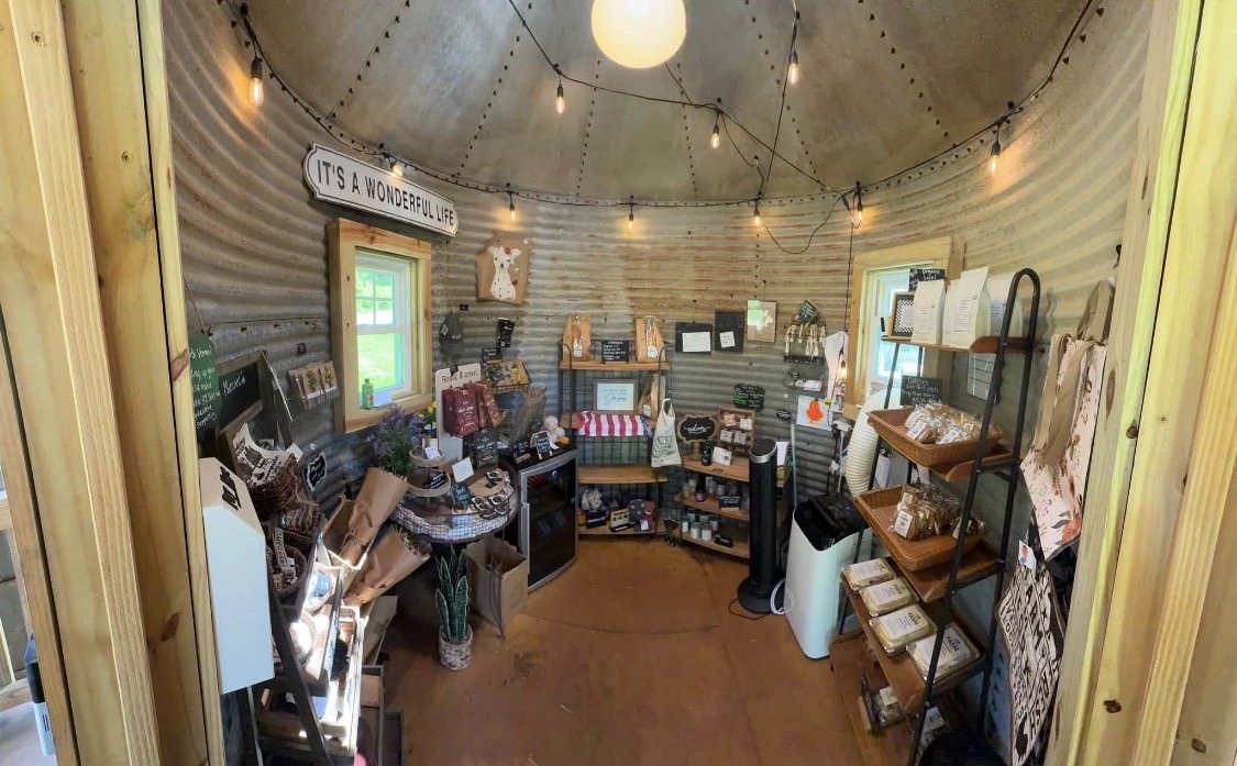 Inside the silo stand: corrugated metal walls, string lights, shelves of baked goods, jars and gifts