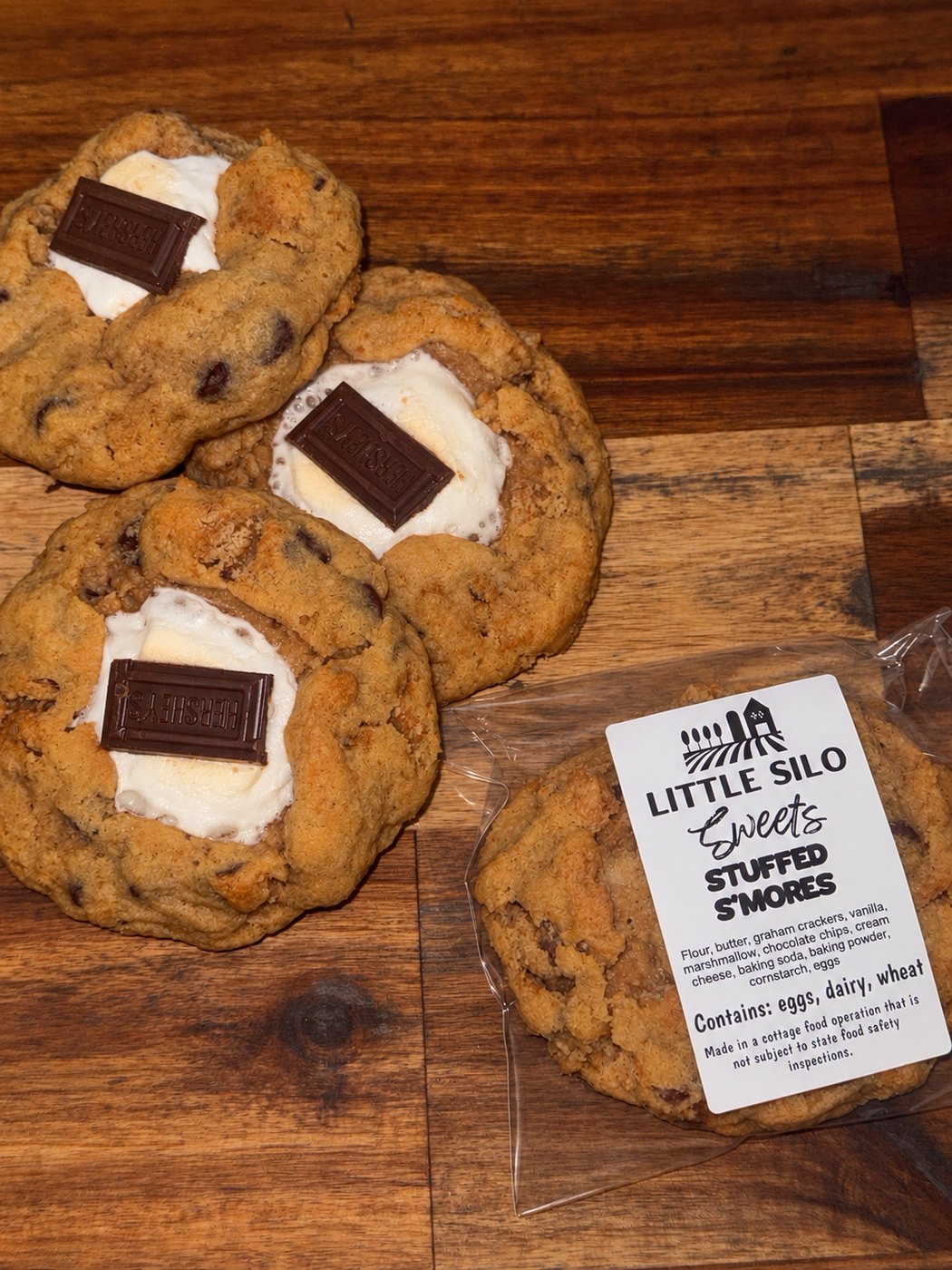 Stuffed s'mores cookies topped with toasted marshmallow and a Hershey's chocolate square, one wrapped with a Little Silo Sweets label